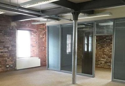 Open office space featuring exposed brick walls, industrial steel beams, and glass partitions.