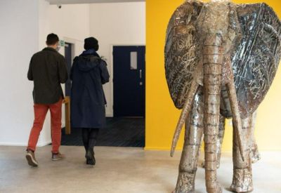 Modern lobby area with a large elephant sculpture and two people walking towards a doorway.
