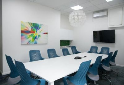 Bright meeting room with a long white table, blue ergonomic chairs, and colorful abstract wall art.