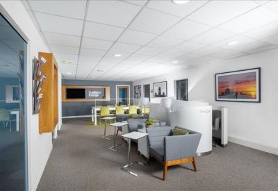 Spacious breakout lounge with grey armchairs and private working pods.