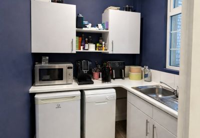 Compact modern kitchenette featuring white cabinetry, a microwave, and blue feature walls.
