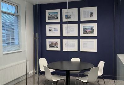 Modern glass-walled meeting room with a round table and framed architectural photos on a navy wall.