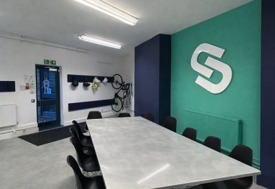 Spacious meeting room with a large white table and a teal feature wall displaying a logo.