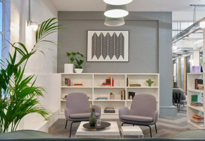 Lounge area with grey armchairs, a white bookshelf, and a large plant.
