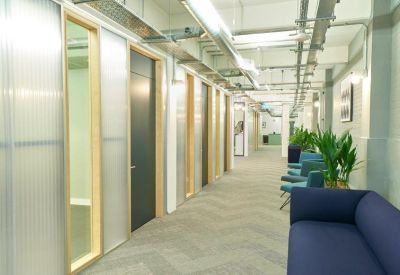 Bright hallway with glass-partitioned offices and a blue sofa.