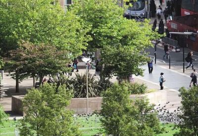 View of a nearby public square with green trees, benches, and pedestrians.
