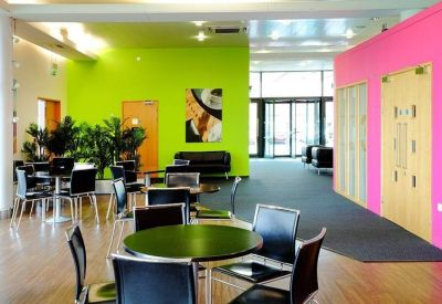 Vibrant communal breakout area featuring lime green and pink feature walls with cafe seating and plants.
