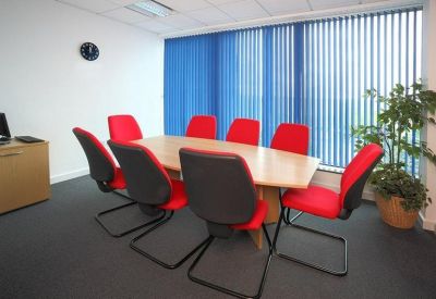Bright meeting room with a light wood table, red and black chairs, and blue vertical blinds.