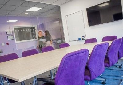 Long conference table with purple chairs and a wall-mounted TV.