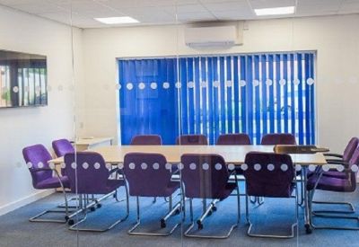 Meeting room featuring a long table, purple chairs, and blue vertical blinds.
