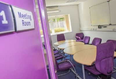 Small meeting room with multiple light wood oval tables and purple seating.