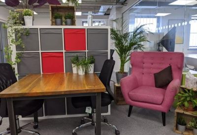 Breakout space with a wooden table, pink armchair, and storage units with red accents.