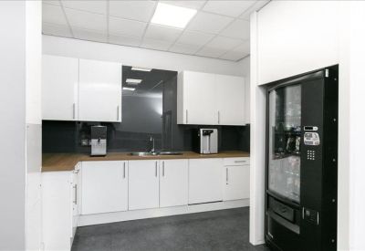 Modern kitchen and break area with white cabinetry and a vending machine.