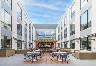 Outdoor communal terrace with contemporary seating, wooden pergolas, and a bar area under a blue sky.
