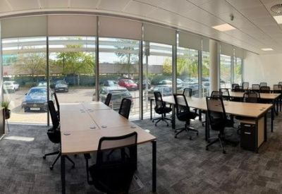 Spacious open-plan office with multiple workstations and large windows overlooking a parking area.