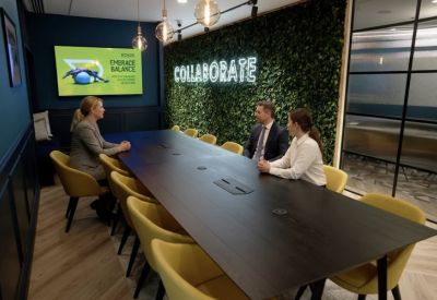 Conference room with a dark wood table, yellow chairs, and a living moss wall featuring neon signage.