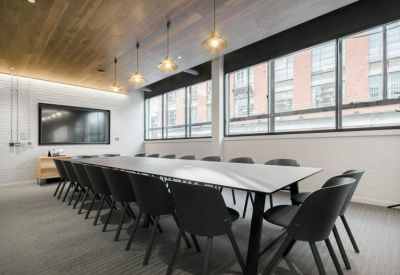 Long boardroom table in a bright room with pendant lighting and large windows.