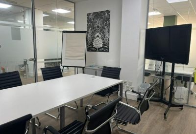Bright meeting room with a white conference table, black chairs, and a large wall-mounted screen.