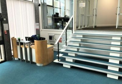 Reception area with a wooden desk and a modern staircase over teal carpeting.