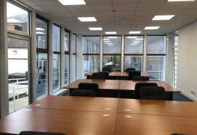 Open-plan office with rows of wooden desks and large floor-to-ceiling windows.