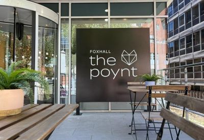 Outdoor terrace entrance with a branded black sign and wooden patio furniture.