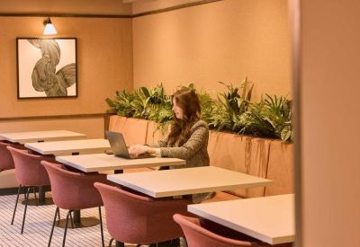 Cozy cafe-style seating area with pink velvet chairs and indoor plants against a warm wall.