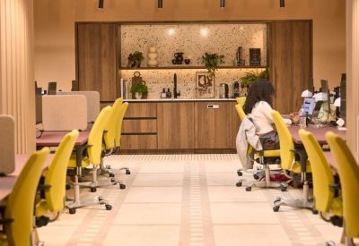 Modern coworking space with ergonomic yellow chairs and a wooden kitchenette background.