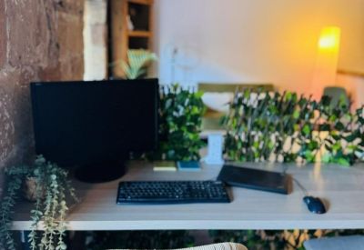 Modern workspace featuring a wicker chair, computer setup, and greenery-covered privacy screens.