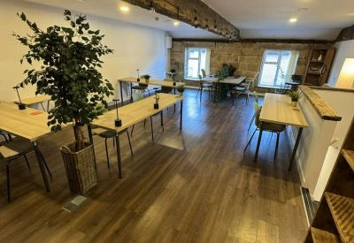 Spacious open-plan office with light wood desks, a large potted tree, and polished floors.