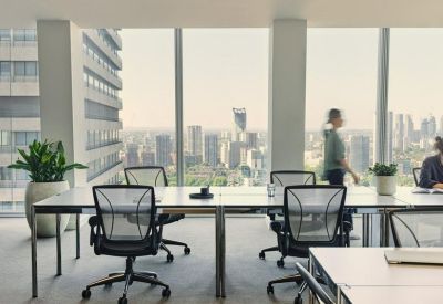 Sleek coworking area with long white desks and floor-to-ceiling windows overlooking the city.