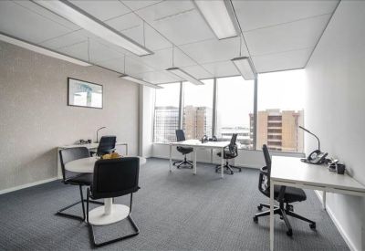 Spacious corner office with multiple desks, black chairs, and large windows.