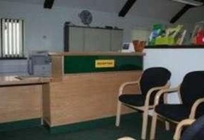 Wooden reception desk with a green front panel and black waiting chairs.
