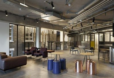 Modern communal lounge with leather sofas, blue drum stools, and industrial-style exposed ceilings.