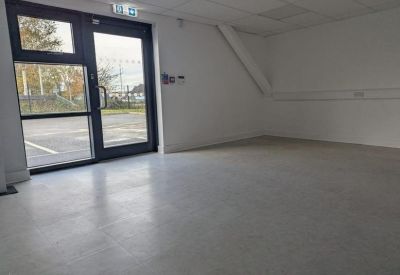Spacious empty room with a glass door leading to a parking area.