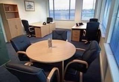 Bright office space featuring a round meeting table and two workstations by large windows.