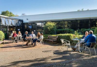 Outdoor patio area with people seated at tables near a modern building facade.