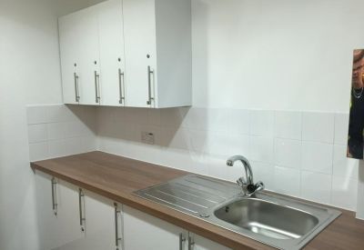 Clean and modern communal kitchenette with white cabinetry and wooden counters.
