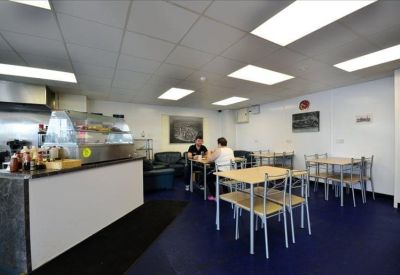 Communal kitchen and dining area with cafe tables, blue flooring, and a serving counter.