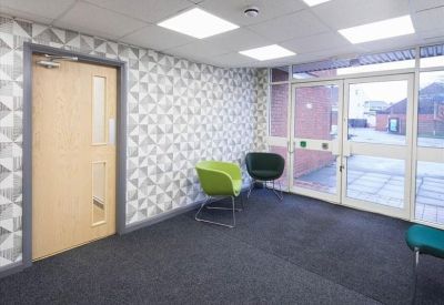 Bright reception area with geometric pattern wallpaper, lime green chair, and glass entrance doors.