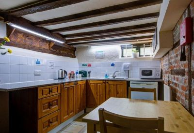 Communal kitchen and dining area with wooden cabinetry and exposed ceiling beams.