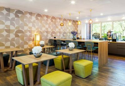 Stylish communal cafe area with geometric wallpaper, wooden tables, and bright lime green stools.