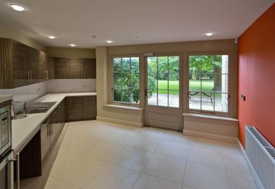 Modern communal kitchen with a bright orange feature wall and garden views through large windows.