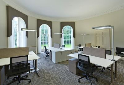 Bright open-plan office space featuring desks with individual floor lamps and large arched windows.
