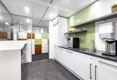 Sleek office kitchen with white cabinetry, green backsplash, and a breakfast bar.