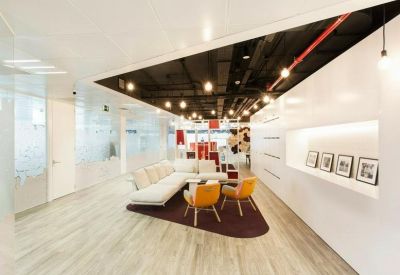 Modern reception lounge with a white sofa, orange chairs, and recessed ceiling lights.
