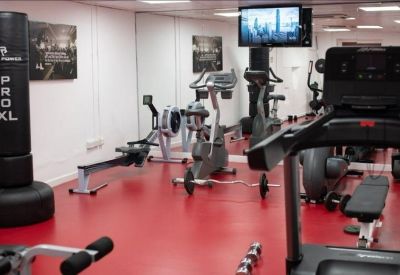 Modern basement gym facility with red flooring, rowing machines, exercise bikes, and a treadmill.
