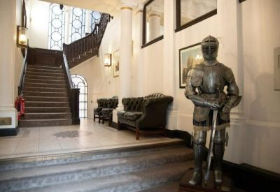 Grand entrance lobby featuring a full suit of armor, dark wood staircase, and leather tufted sofas.