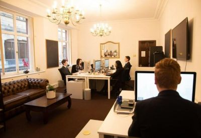 Bright shared office space with chandeliers, a leather sofa, and professionals working at white desks.