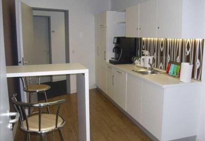 Modern office kitchen and breakout area with white cabinetry and bar seating.