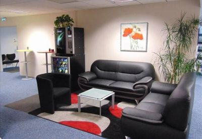 Modern communal lounge featuring black leather sofas, a colorful rug, and a coffee machine.